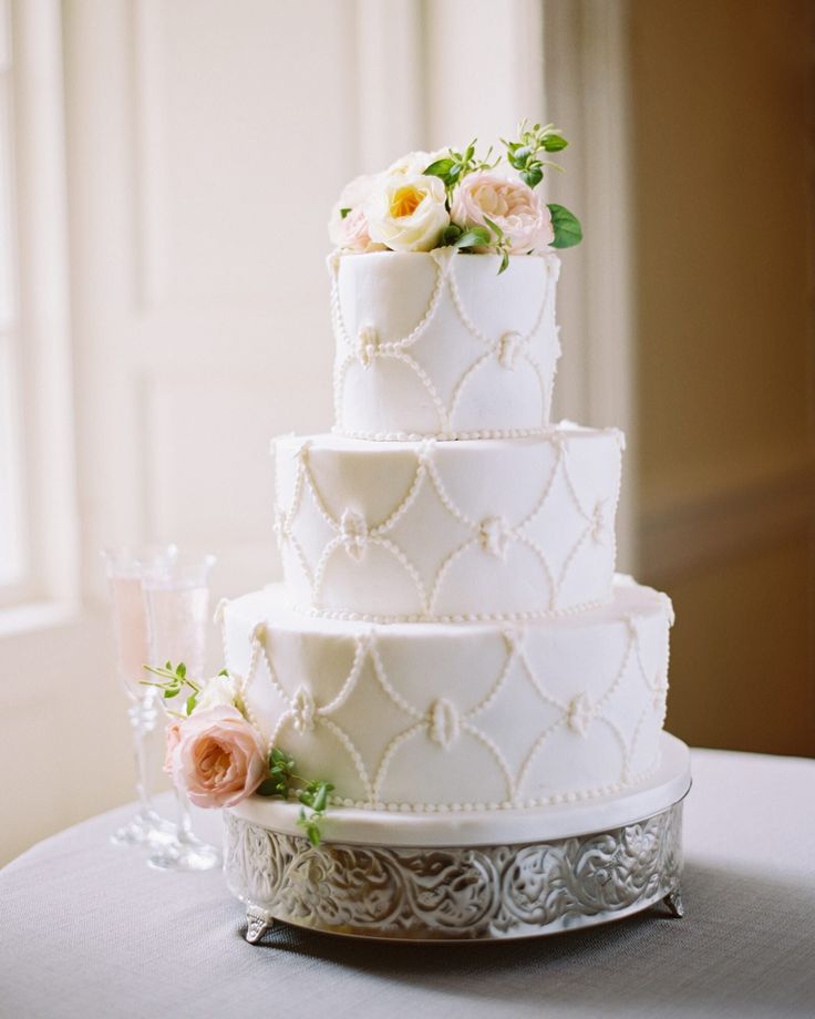 a three tiered wedding cake with flowers on the top is sitting on a table