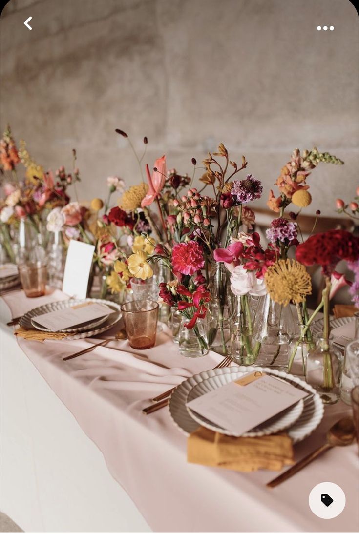 the table is set with flowers and place settings for guests to sit down at it