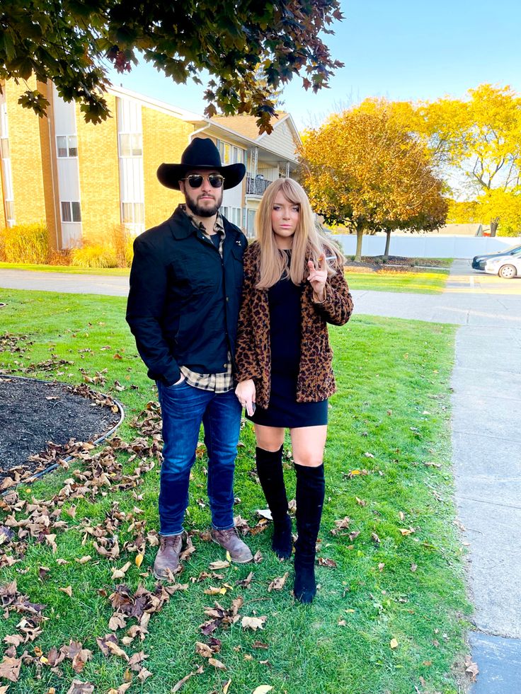 a man and woman standing in front of a building wearing cowboy hats, jeans and boots