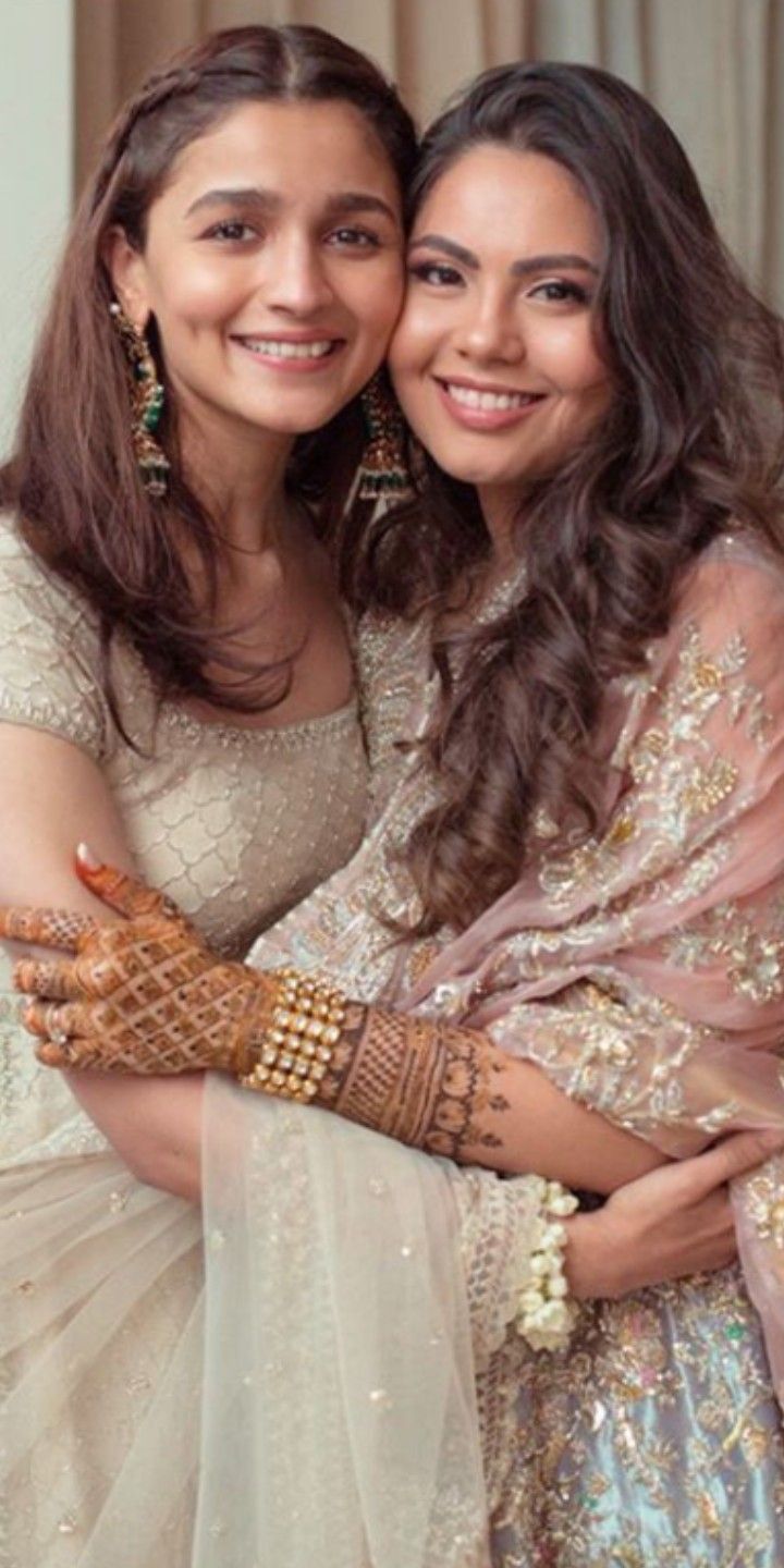 two young women hugging each other in their wedding outfits, both dressed in white and gold