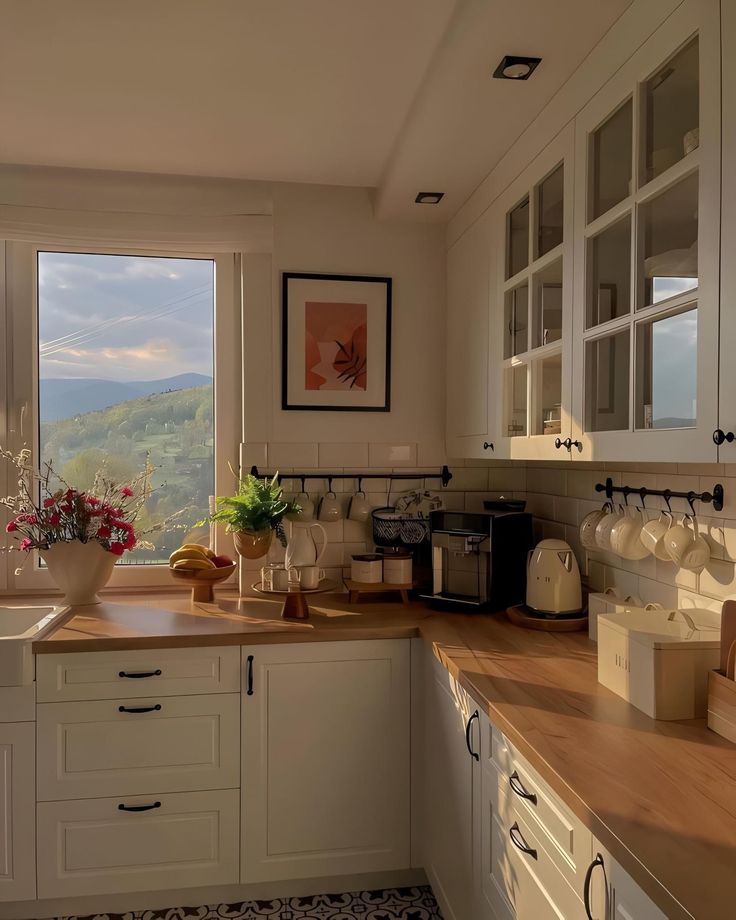 a kitchen with white cabinets and wooden counter tops next to a window overlooking the mountains