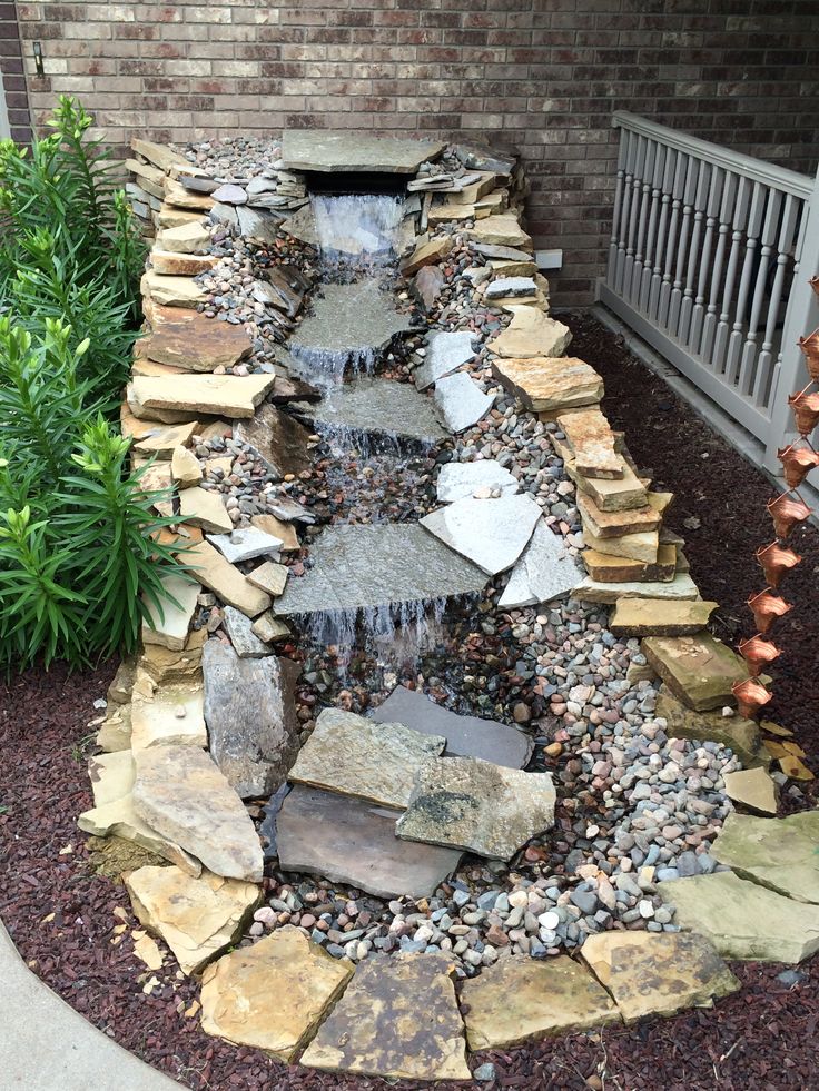 a small waterfall in the middle of a rock and gravel garden bed with rocks around it