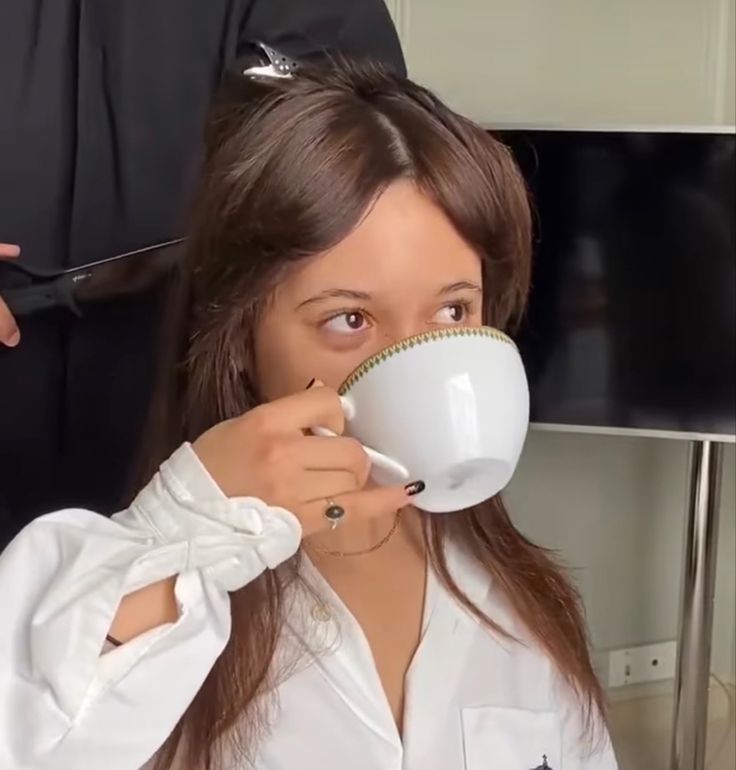 a woman is getting her hair done while holding a coffee cup in front of her face