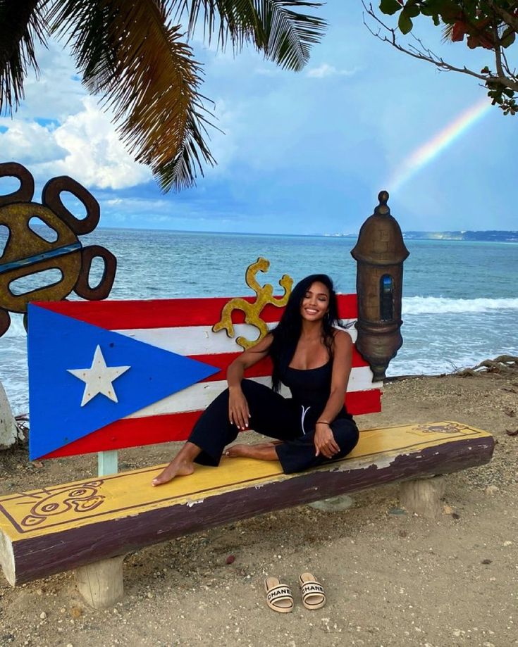 a woman sitting on a bench in front of the ocean with a flag painted on it