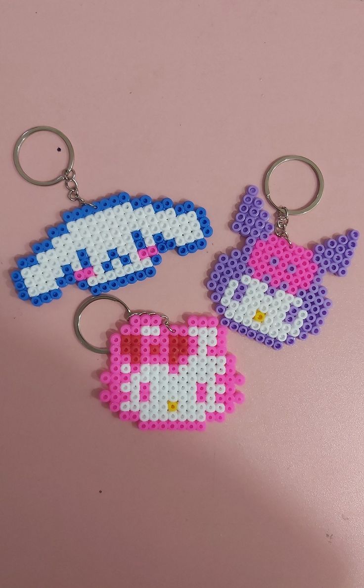 three keychains made out of perler beads on a pink surface, one has an image of hello kitty and the other has a heart