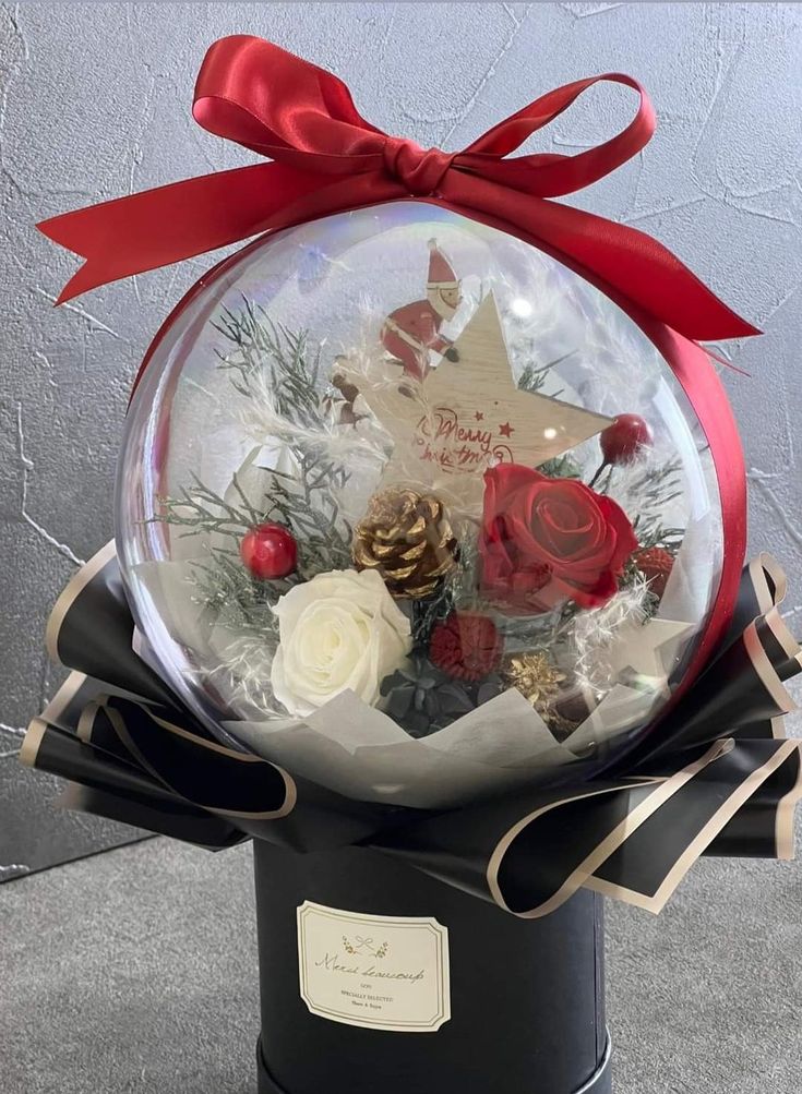 a snow globe with roses and pine cones in it on top of a black box