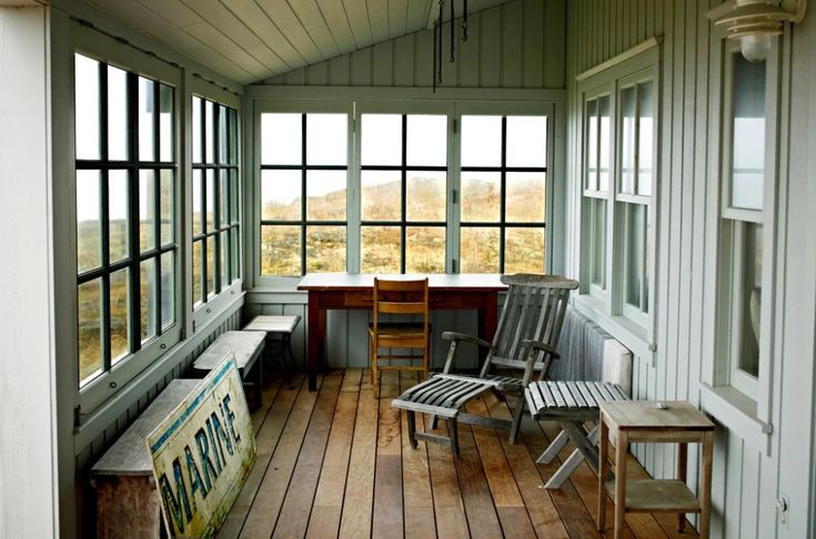 an empty porch with two chairs and a table on the far side, in front of large windows