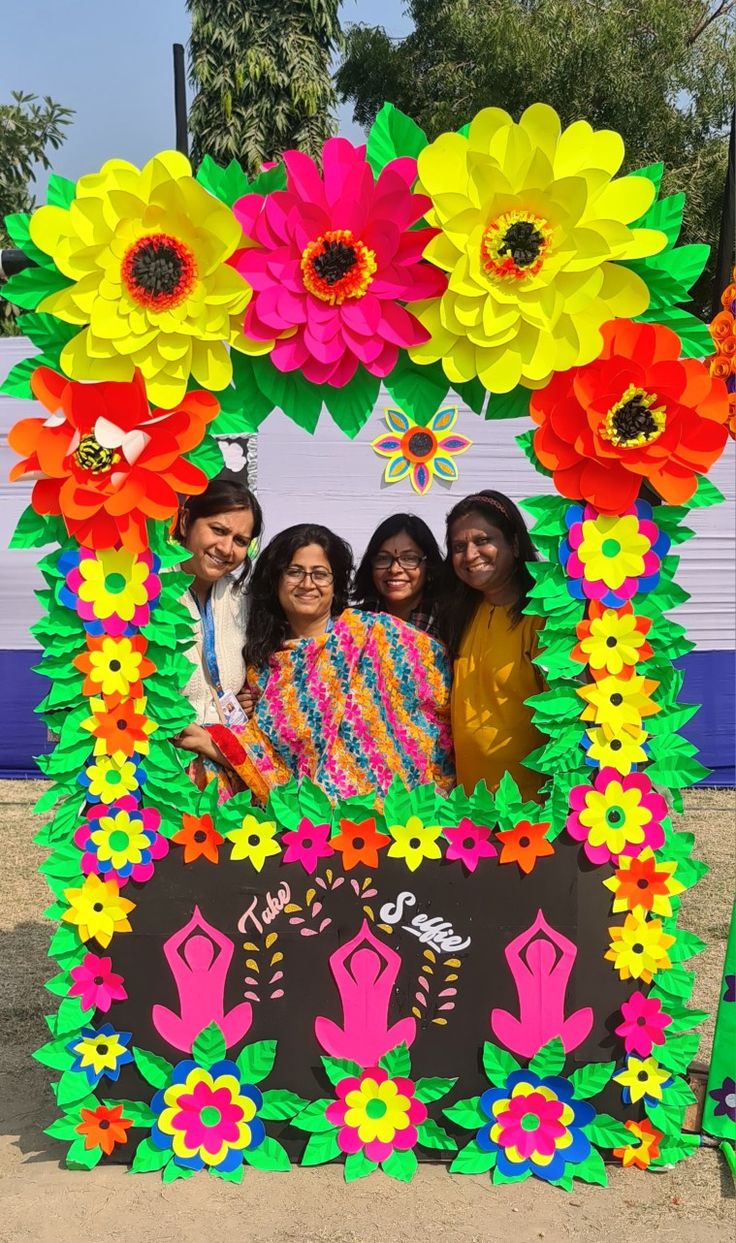 three women standing in front of a colorful display with paper flowers on the sides and one woman holding a book