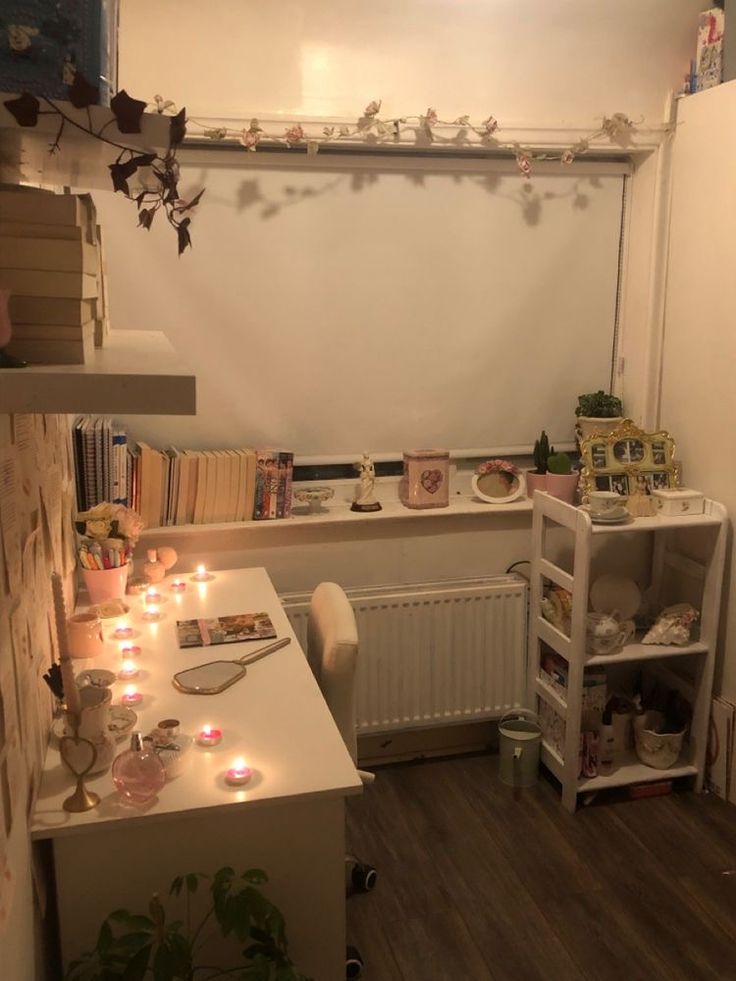 a small room with many books and candles on the desk, in front of a white wall