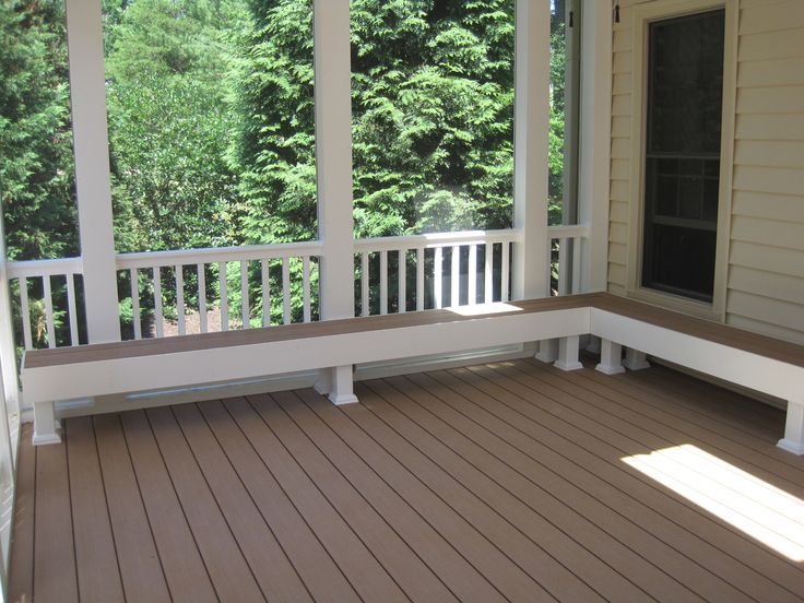 a porch with wooden flooring and white railings on both sides, looking out onto the trees