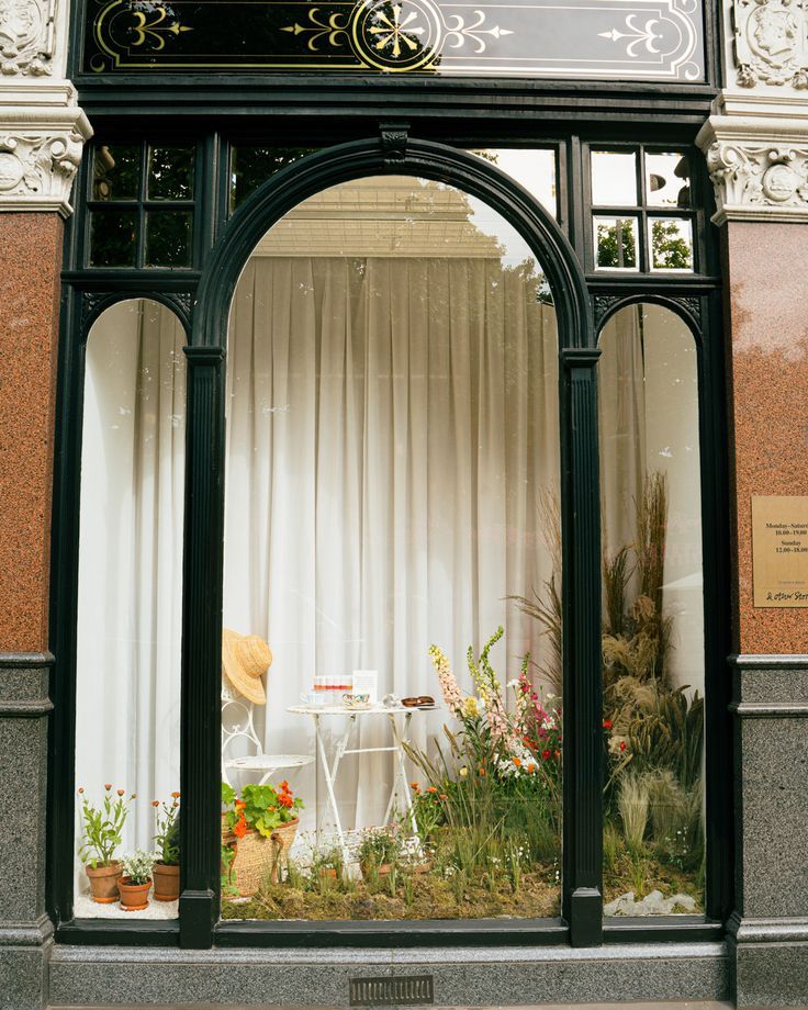 a store front with an arched window and flower display in the middle, along with white drapes