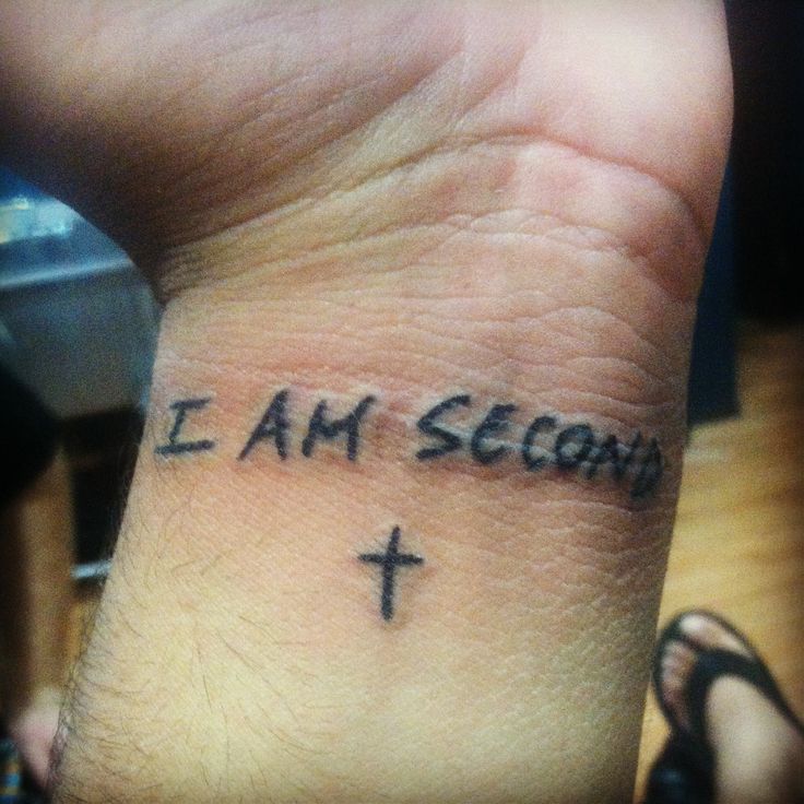 a person with a tattoo on their wrist that says i am second and the cross is in black ink