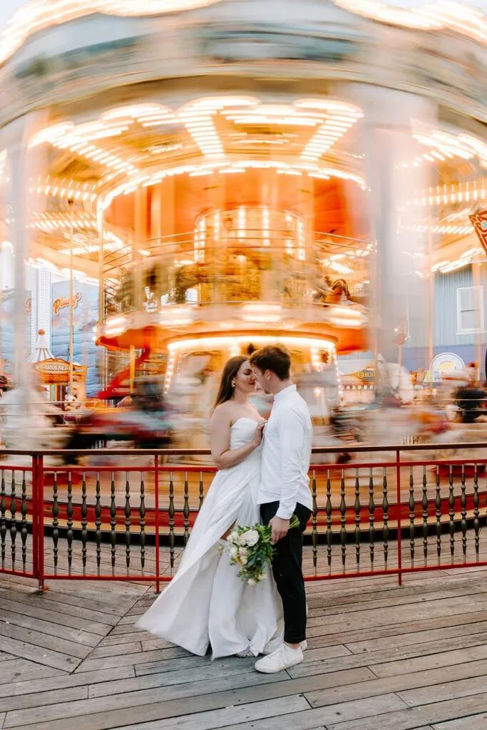 a bride and groom standing in front of a merry go round at a fairground