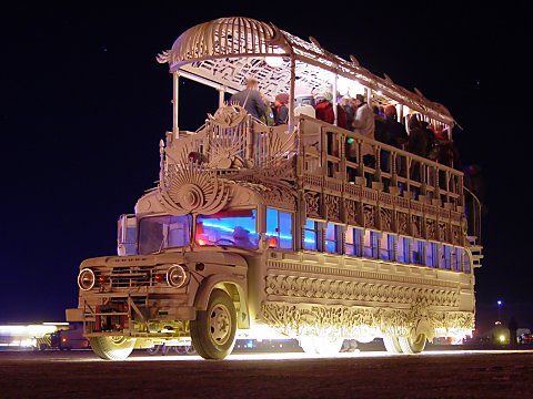 a large bus with people on top driving down the street at night time in front of a building