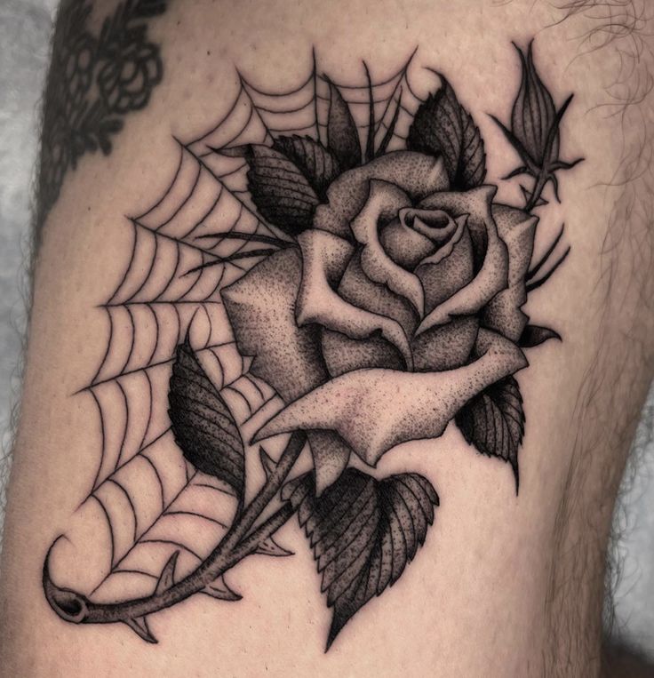 a black and white rose tattoo on the thigh with spiderwetches around it