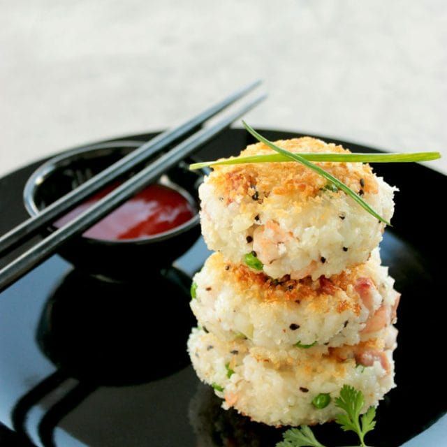 two crab cakes on a black plate with chopsticks