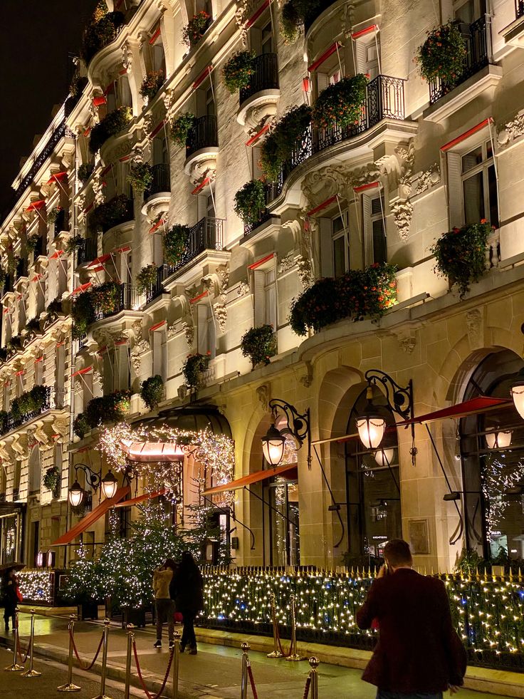 people are walking down the street in front of a building with christmas lights on it