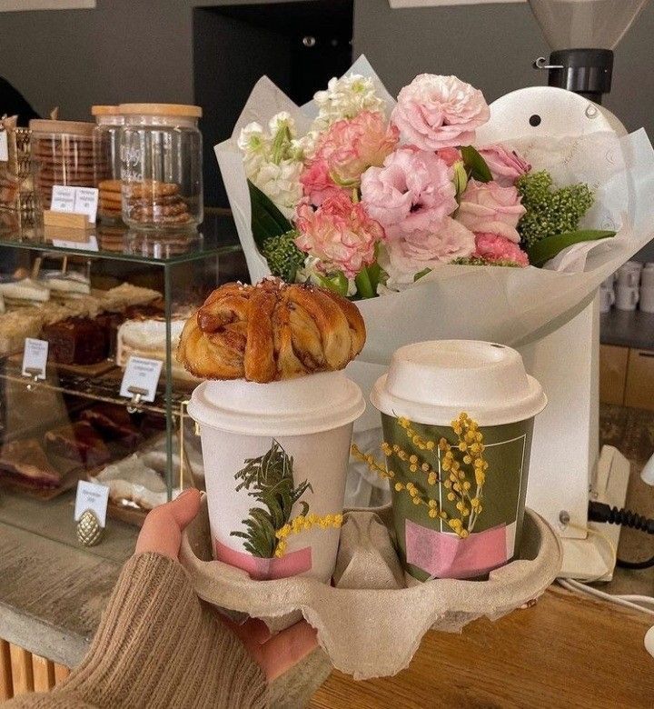 a person holding two cups with pastries on them in front of a bakery counter