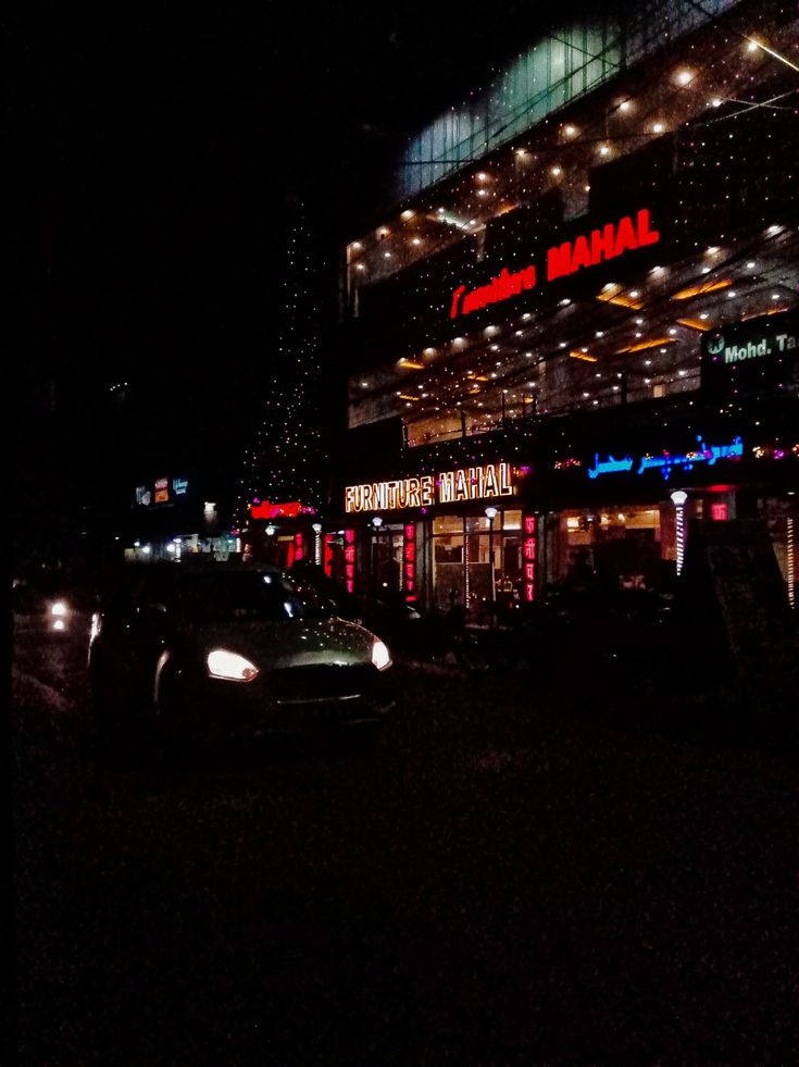 a car parked in front of a building with lights on it's sides at night