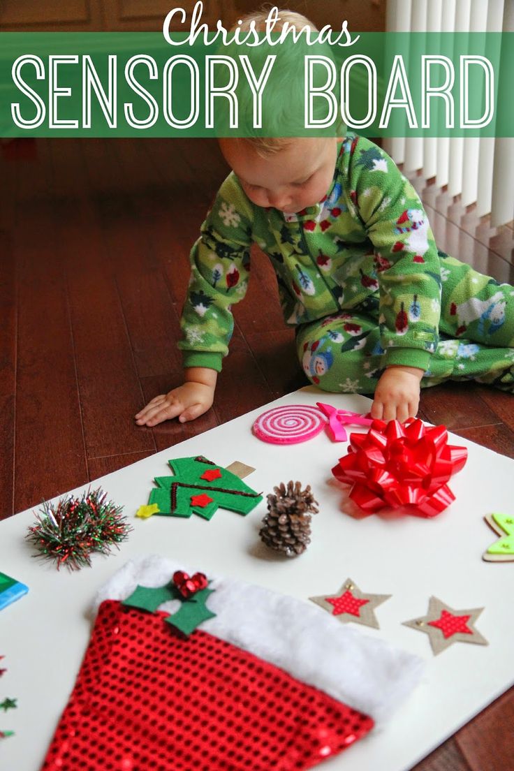 a baby in pajamas playing with christmas decorations on the floor next to a white board