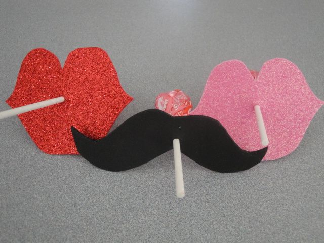 two mustaches with candy sticks sticking out of them on top of a gray surface