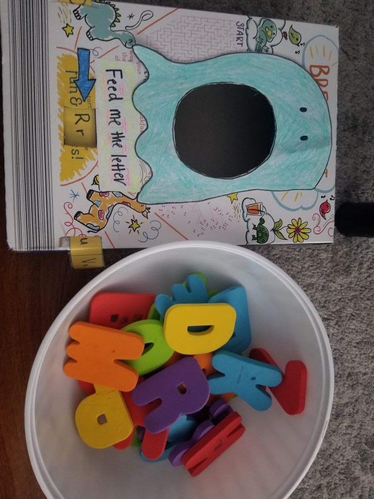 a white bowl filled with plastic letters next to a children's book on the floor