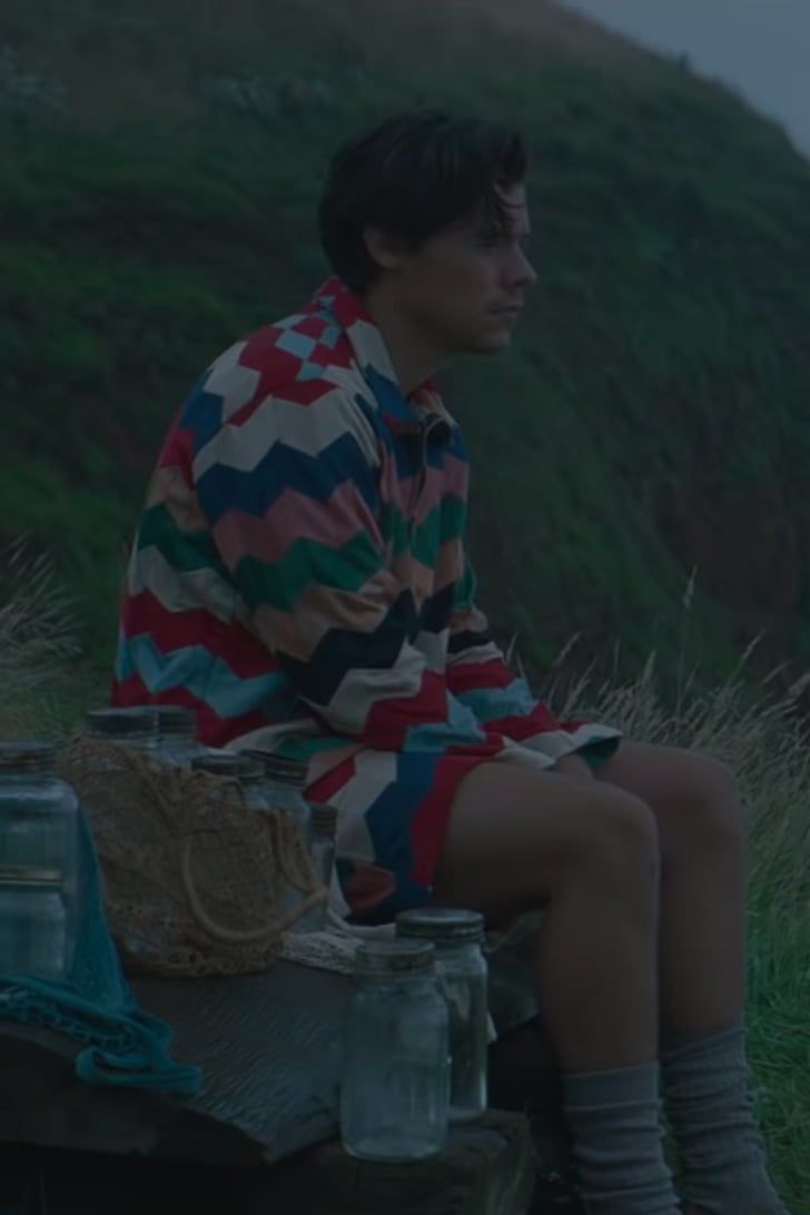 a young man sitting on top of a wooden bench next to a green hillside covered in grass