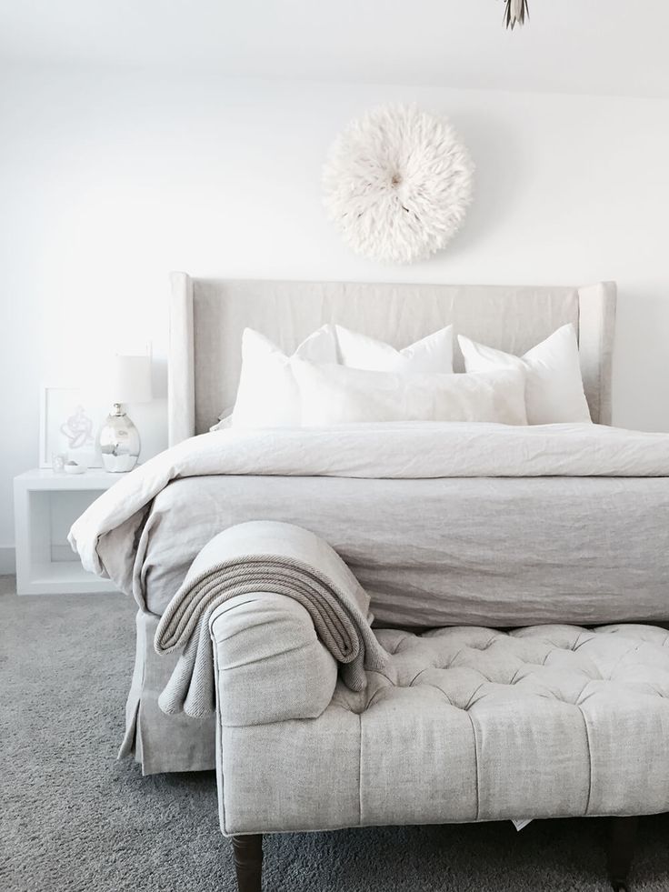 a bedroom with a bed, ottoman and chandelier hanging above the headboard