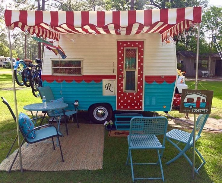 an old camper is parked in the grass with blue chairs and tables underneath it