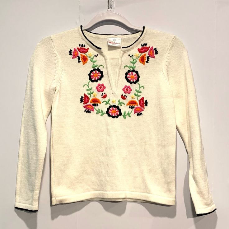 a white sweater with flowers on it hanging from a hanger in front of a wall