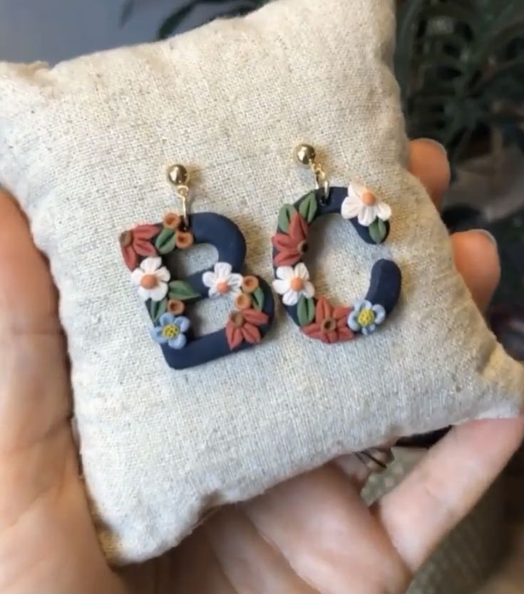 a pair of earrings with flowers on them sitting on a pillow in someone's hand