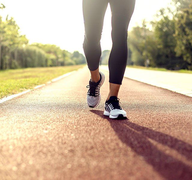 a close up of a person's feet walking down the road with trees in the background