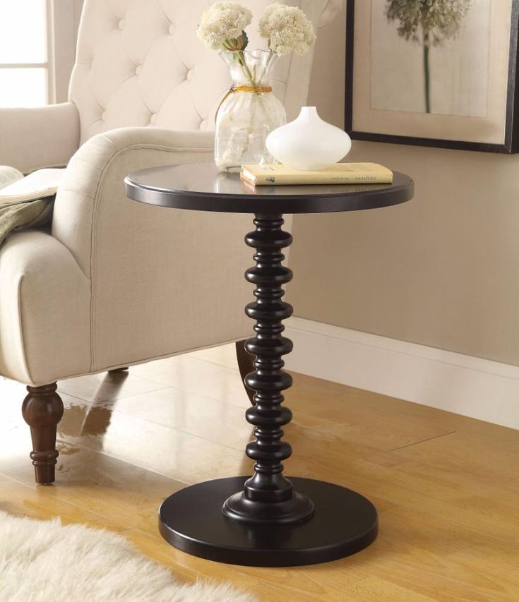 a black table with flowers on it in front of a white chair and framed pictures