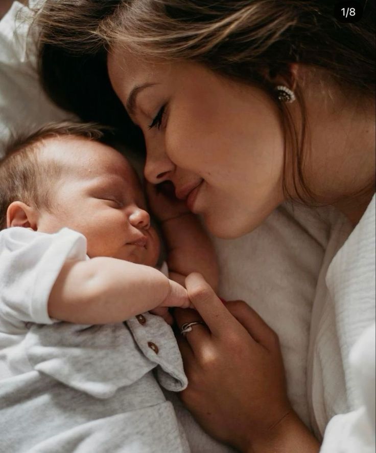 a woman holding a baby in her arms and kissing it's face with both hands