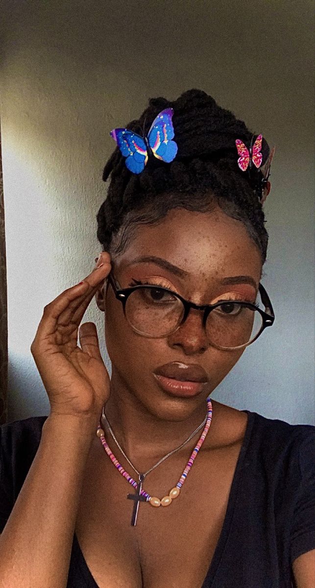 a woman wearing glasses and a necklace with butterflies on it's head is looking at the camera