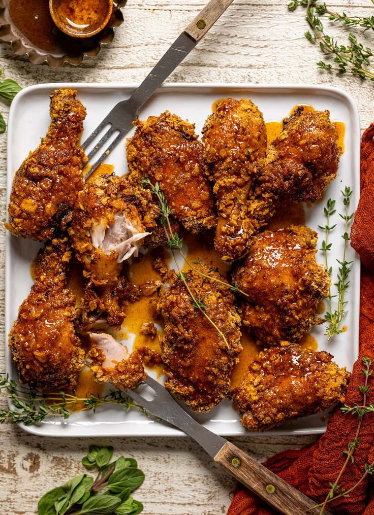 chicken wings with sauce and herbs on a white plate next to a knife and fork