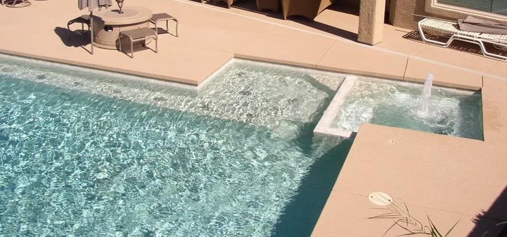 an empty swimming pool next to a patio with chairs and umbrellas on the side