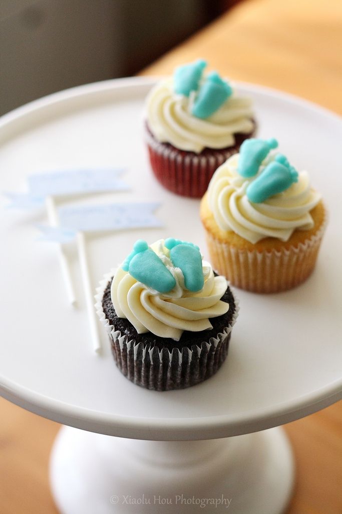 two cupcakes sitting on top of a white cake plate with blue frosting