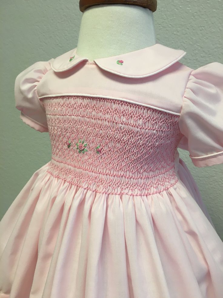 Handsmocked precious pink baby dress adorned with roses.  Peter Pan color and hem of dress also have hand embroidered rosebuds for a precious touch.  Deep bodice smocking, rose floral accent.  Buttons and ties with a bow in the back.  Very full skirt, deep hem.  Machine washable.  Sized for 12-24 months. Pink Fitted Dress With Smocked Cuffs, Fitted Pink Embroidered Smocked Dress, Fitted Pink Smocked Dress With Embroidery, Elegant Pink Dress With Smocked Cuffs, Pink Smocked Dress For Baptism, Fitted Pink Smocked Dress, Pink Smock Dress For Baptism, Pink Fitted Smocked Dress For Baptism, Pink Floral Embroidery Dress For Baptism