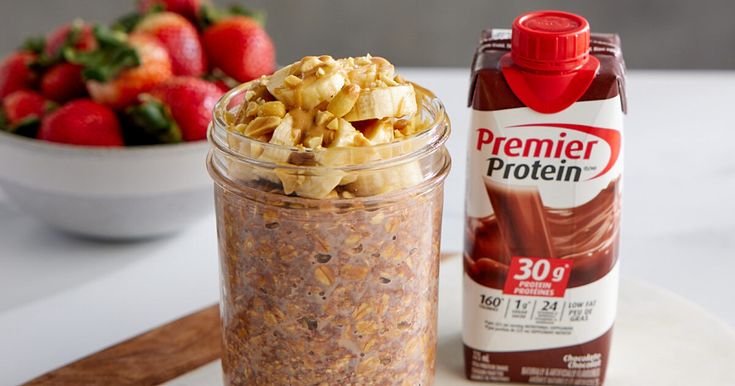 a glass jar filled with cereal next to a bowl of strawberries and a bottle of protein