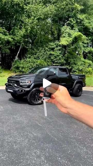 a hand holding a remote control in front of a black truck with trees in the background