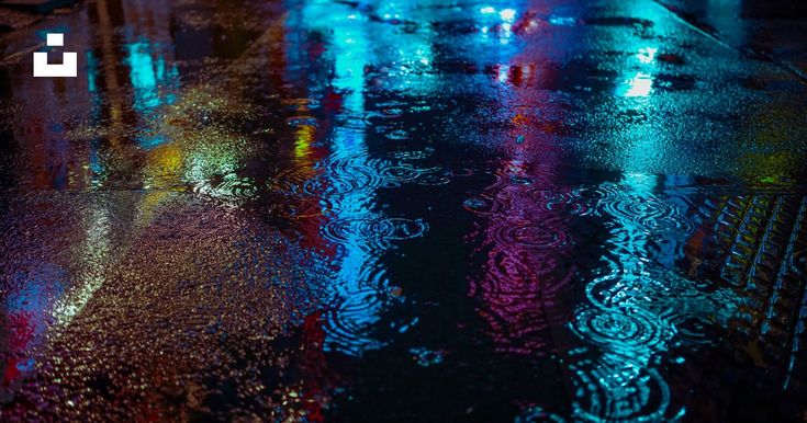 rain drops on the ground at night with street lights reflected in wet pavement and umbrellas