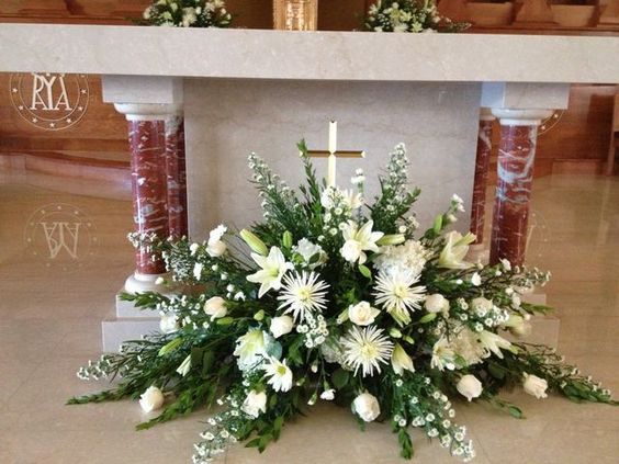 a floral arrangement on the ground in front of a cross at a church altar with candles and flowers