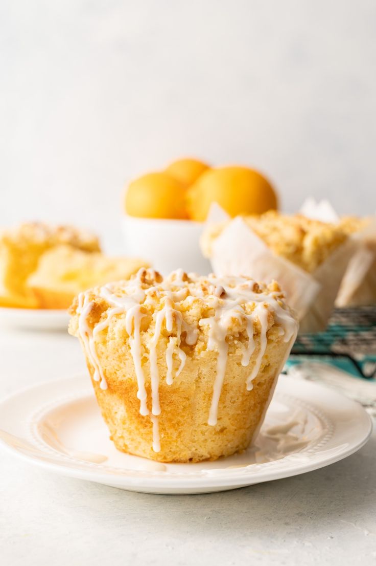 a muffin with icing on a plate next to some oranges in the background