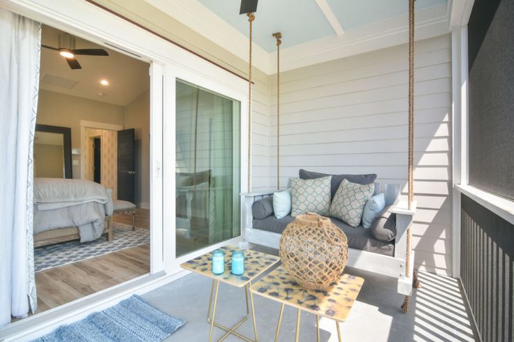 a porch with a swing, table and pillows on it in front of a bedroom