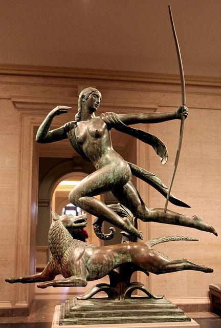 a bronze statue in the shape of a woman holding a bow with two birds around her