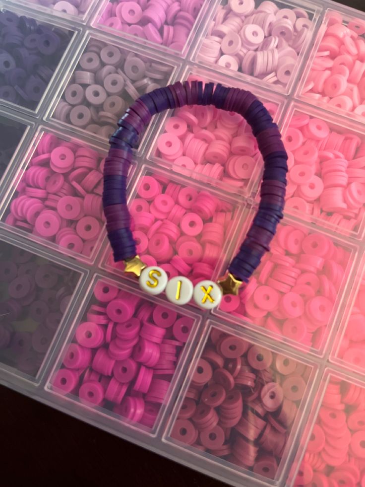 an assortment of beads are displayed in a plastic case on a pink and purple background