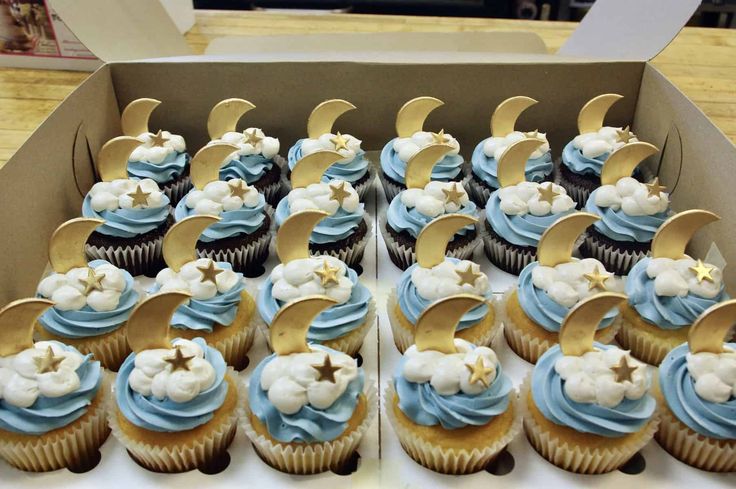 cupcakes with blue frosting and gold moon decorations in a box on a table