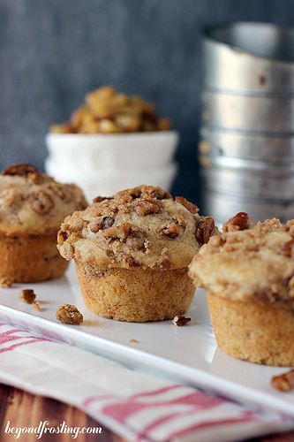 three muffins on a white plate next to bowls of nuts