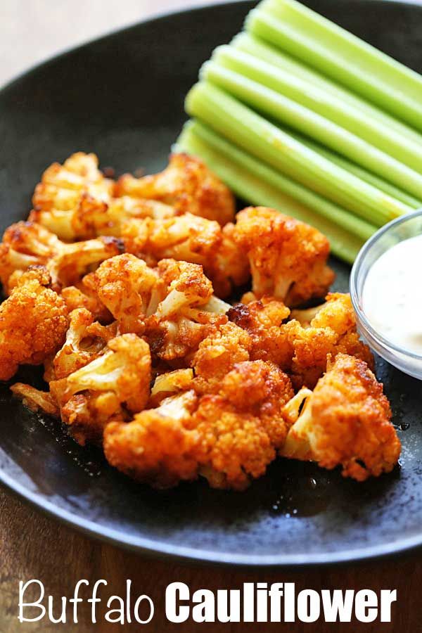 cauliflower and celery on a black plate with ranch dressing next to it